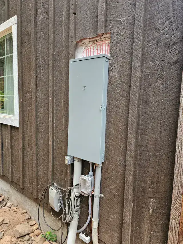 A new meter base and service panel mounted on dark board-and-batten siding