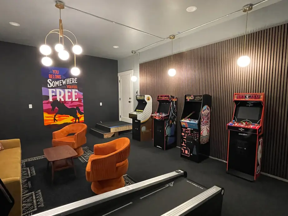 A finished game room with a pendant light cluster, arcade cabinets and a lit slat wall