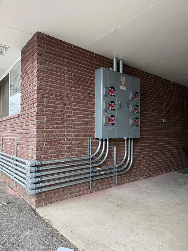 A commercial meter bank and rows of conduit on a brick wall, wired by Wattsmart Electric