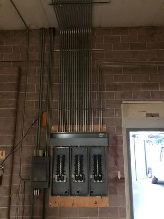 A row of metal conduit risers climbing a brick wall into a set of panels