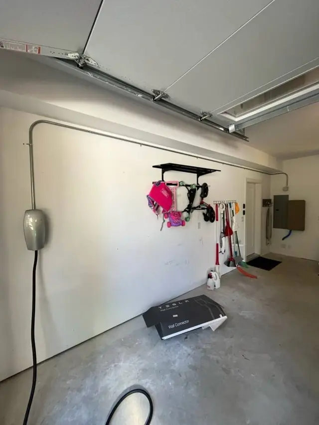 A charger mounted on a finished garage wall with its cable running to the floor