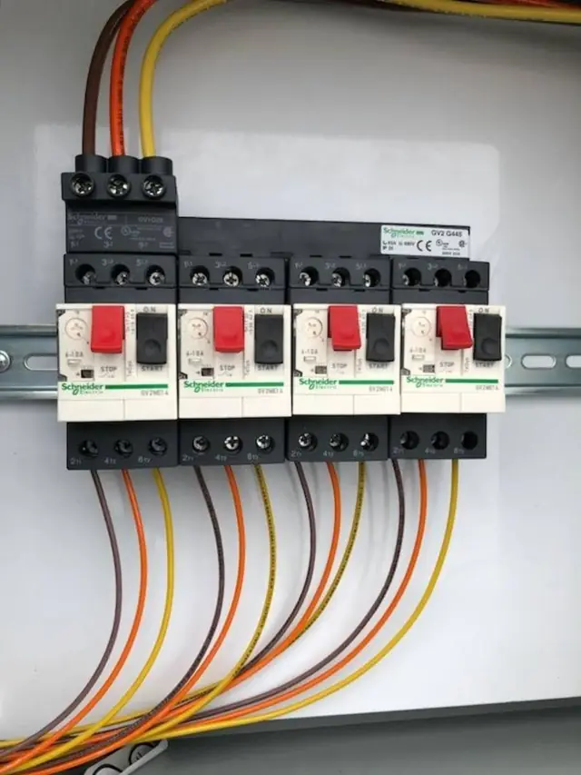 Four motor starters mounted on a rail with orange, yellow and brown wires landing on them