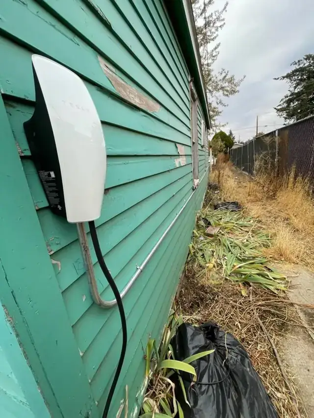 A Tesla Wall Connector mounted on green lap siding beside a driveway